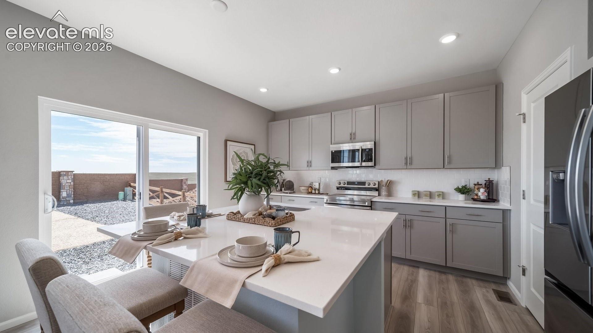 Kitchen featuring an expansive island with a solid surface countertop, stainless steel appliances, a tile backsplash, and light gray cabinetry
*photos of a model home*