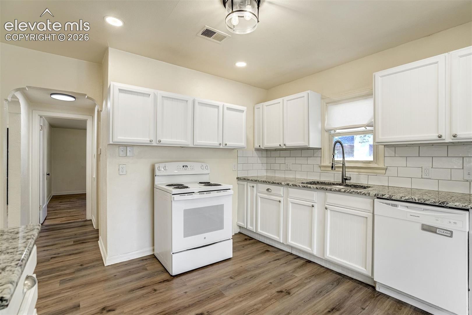 Kitchen featuring white cabinetry, stone-finish countertops, subway tile backsplash, wood-finish flooring, and a stainless steel arched faucet