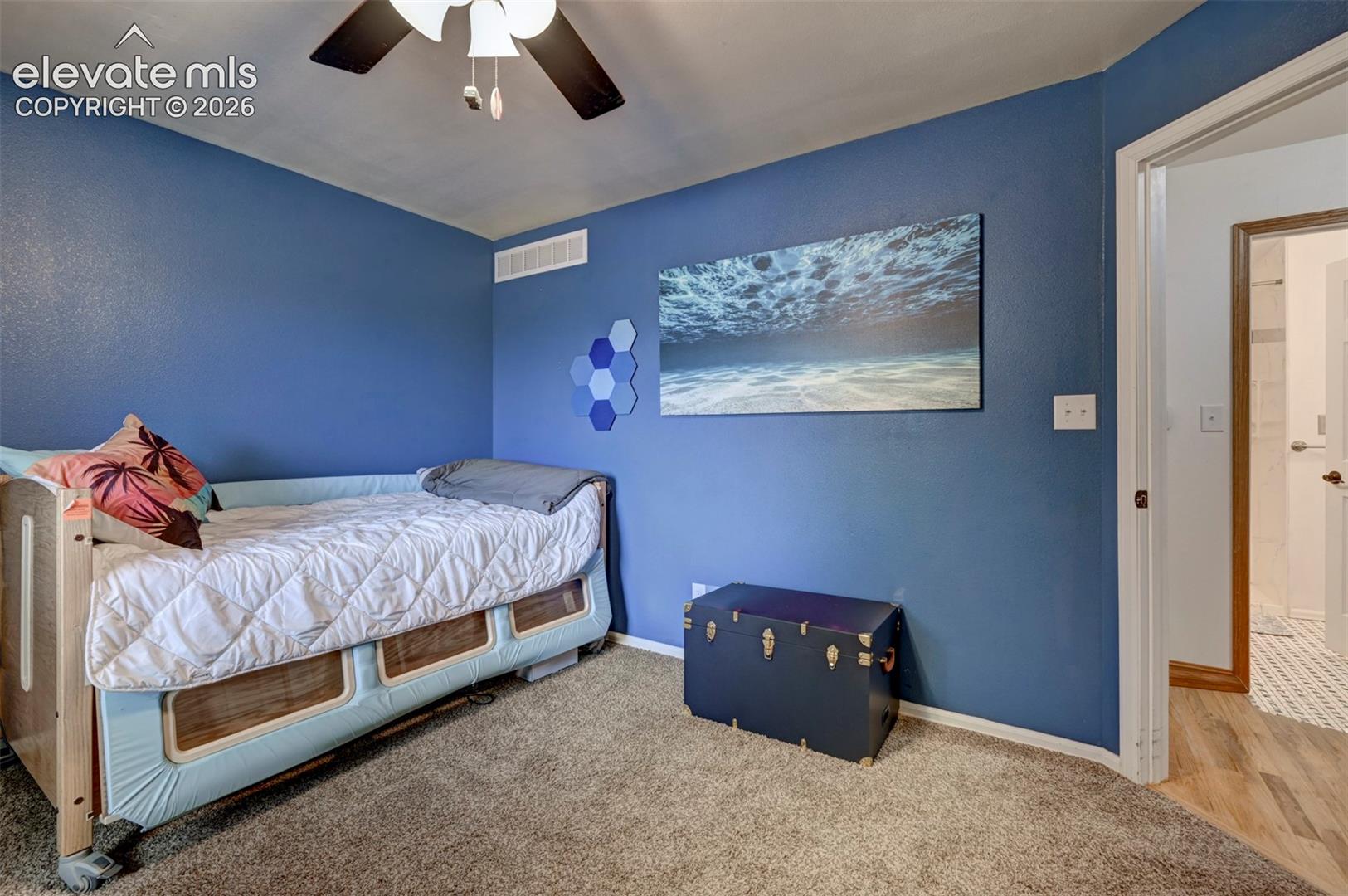 Carpeted flooring, blue painted walls, and a ceiling-mounted fan with integrated lighting