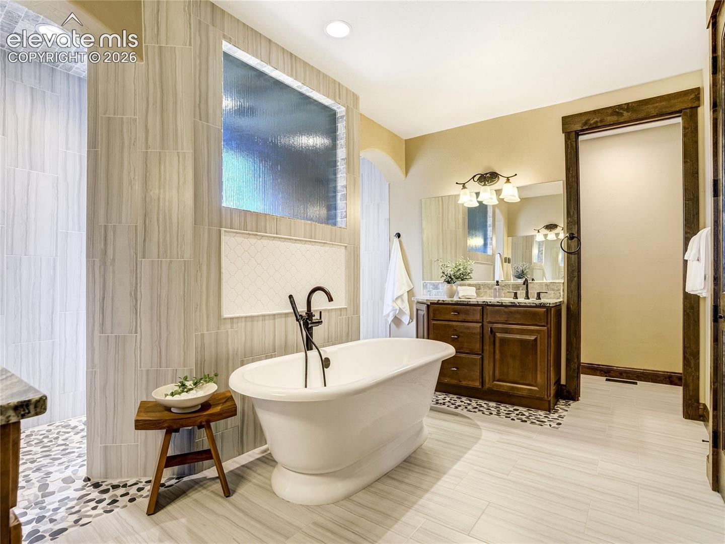 The spa-like primary bath blends refined finishes with thoughtful functionality, featuring split vanity sinks, a freestanding soaking tub, and an expansive walk-in shower.
