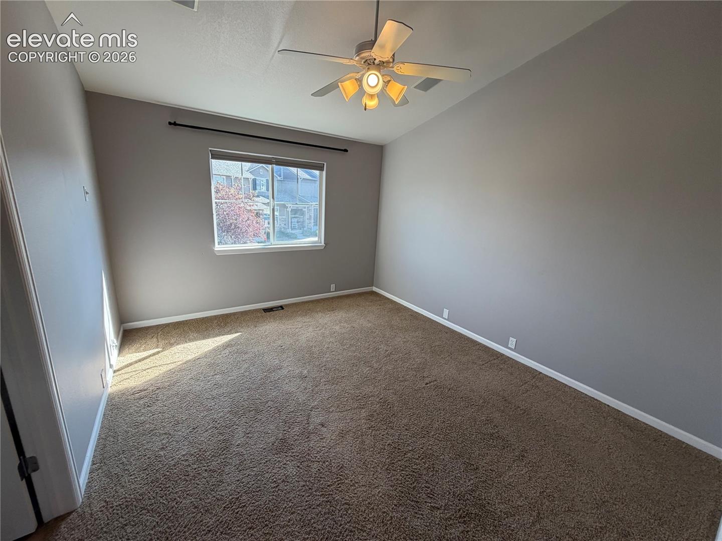 Vaulted ceiling with a ceiling fan light fixture, neutral tone carpeting, and a window with a curtain rod