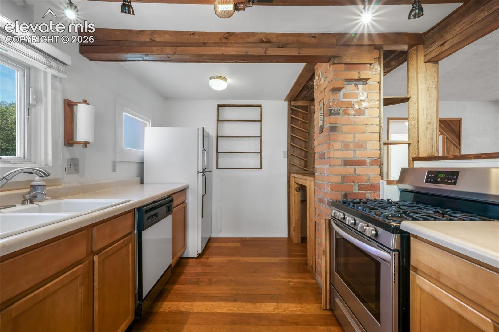 Kitchen featuring wood-finish flooring, exposed wood beams, a brick accent wall, stainless steel range, and a dual basin sink