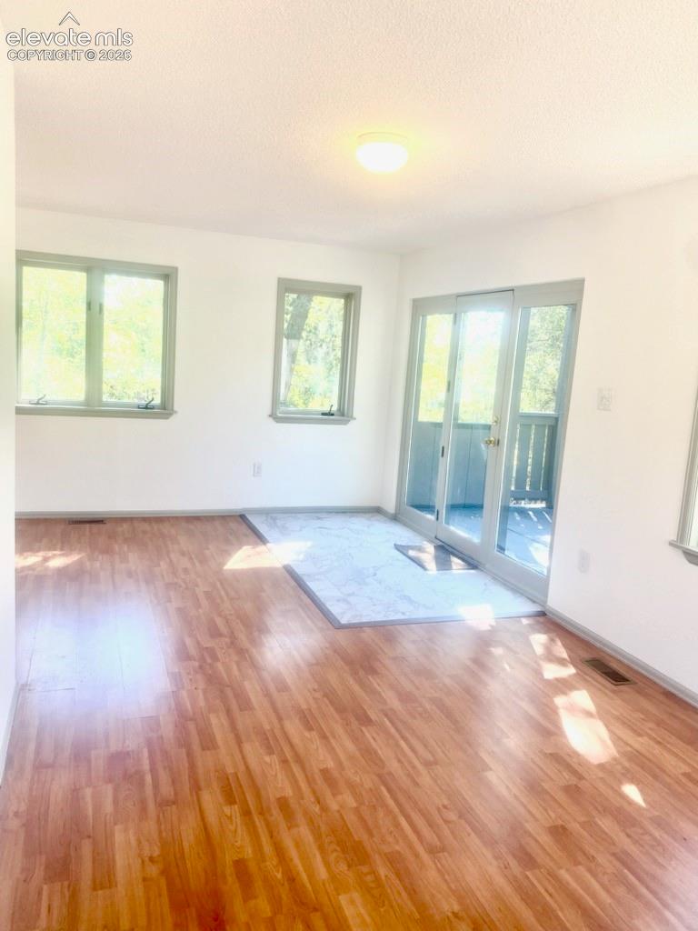 Wood-finish flooring, white walls, two windows, glass sliding doors, and light-toned tile flooring