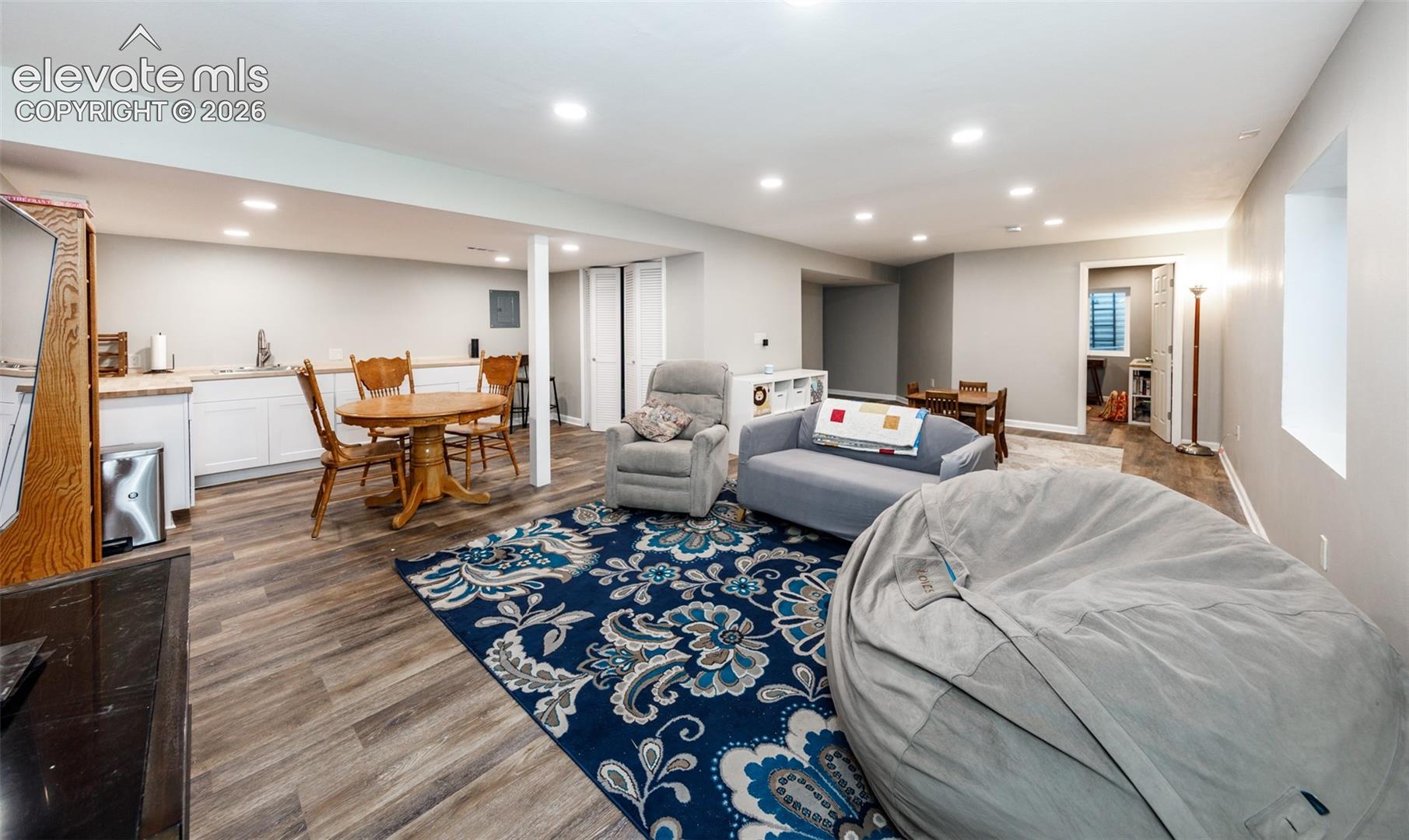 Spacious finished basement with wood-finish flooring, recessed lighting, and a built-in wet bar featuring white cabinetry and light countertops