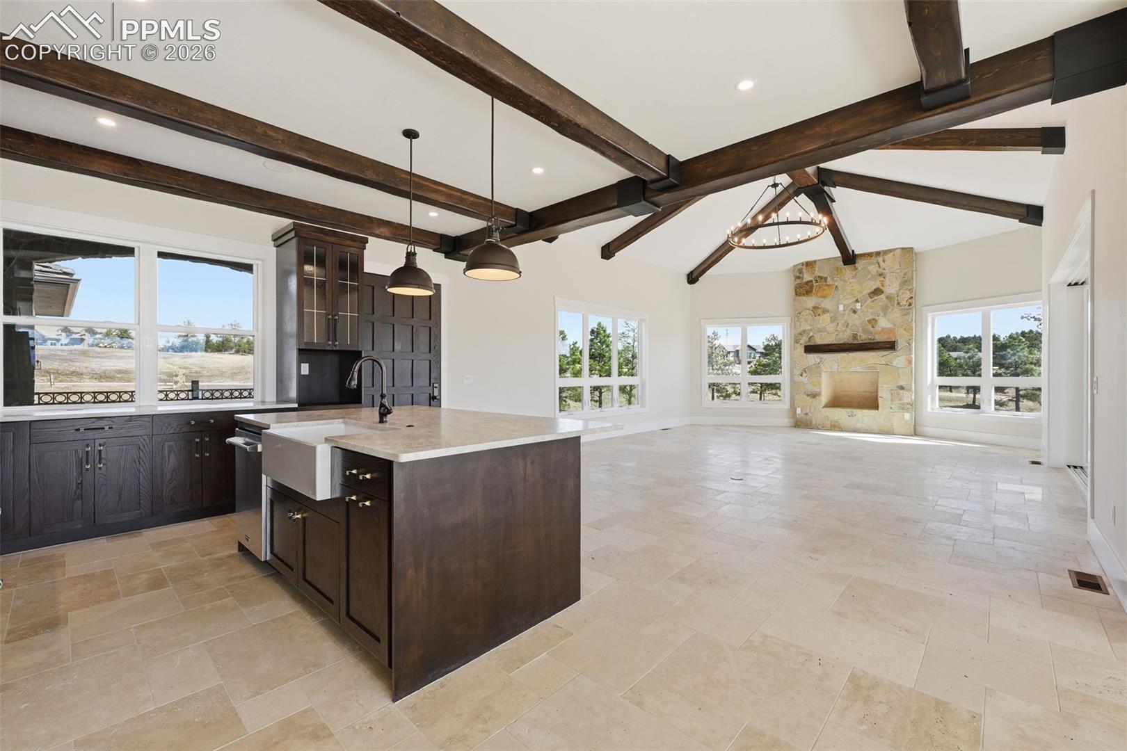Kitchen with dark wood finish cabinets, a kitchen island with sink, open floor plan, stone tile floors, and glass fronted cabinets. Note main entrance to home.