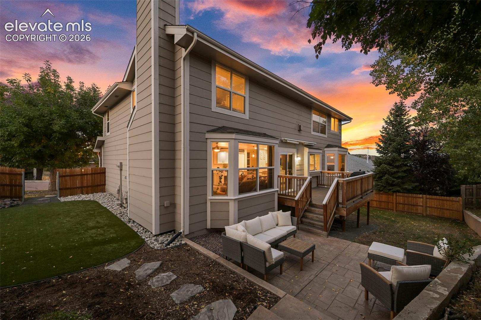 Expansive back exterior with a wood deck, stamped concrete patio, bay windows, and fenced yard