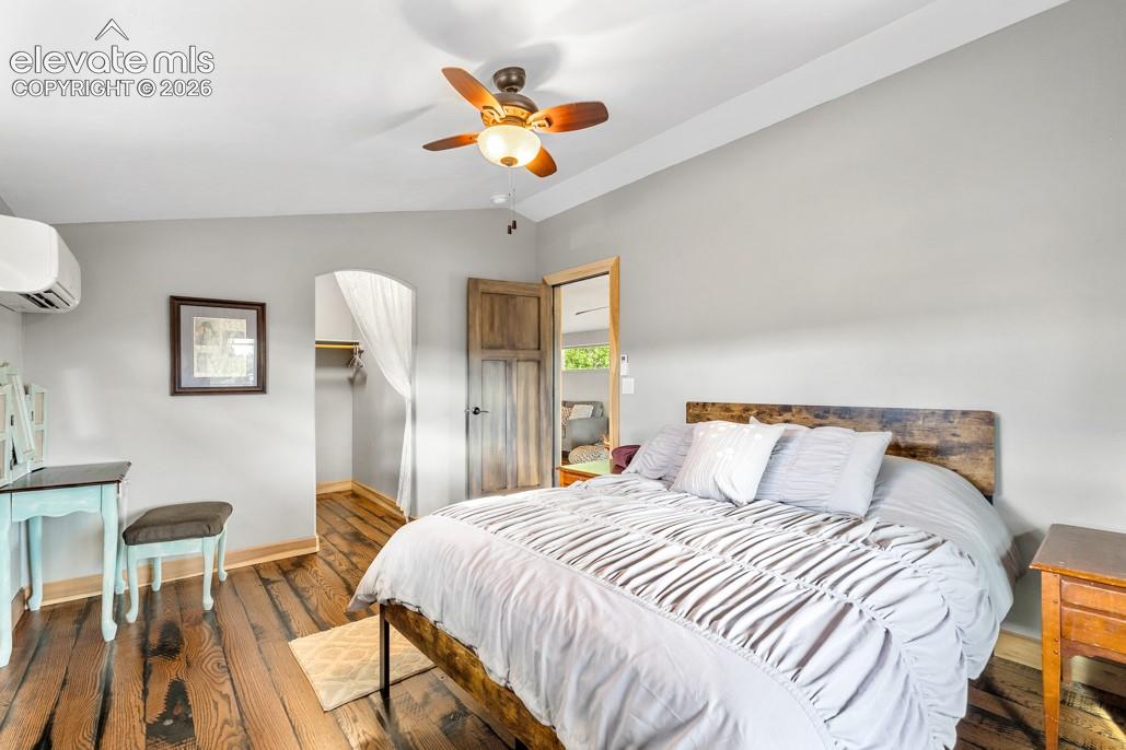 Hardwood flooring, ceiling fan with integrated lighting, mini-split air conditioning unit, arched doorway, and solid wood door