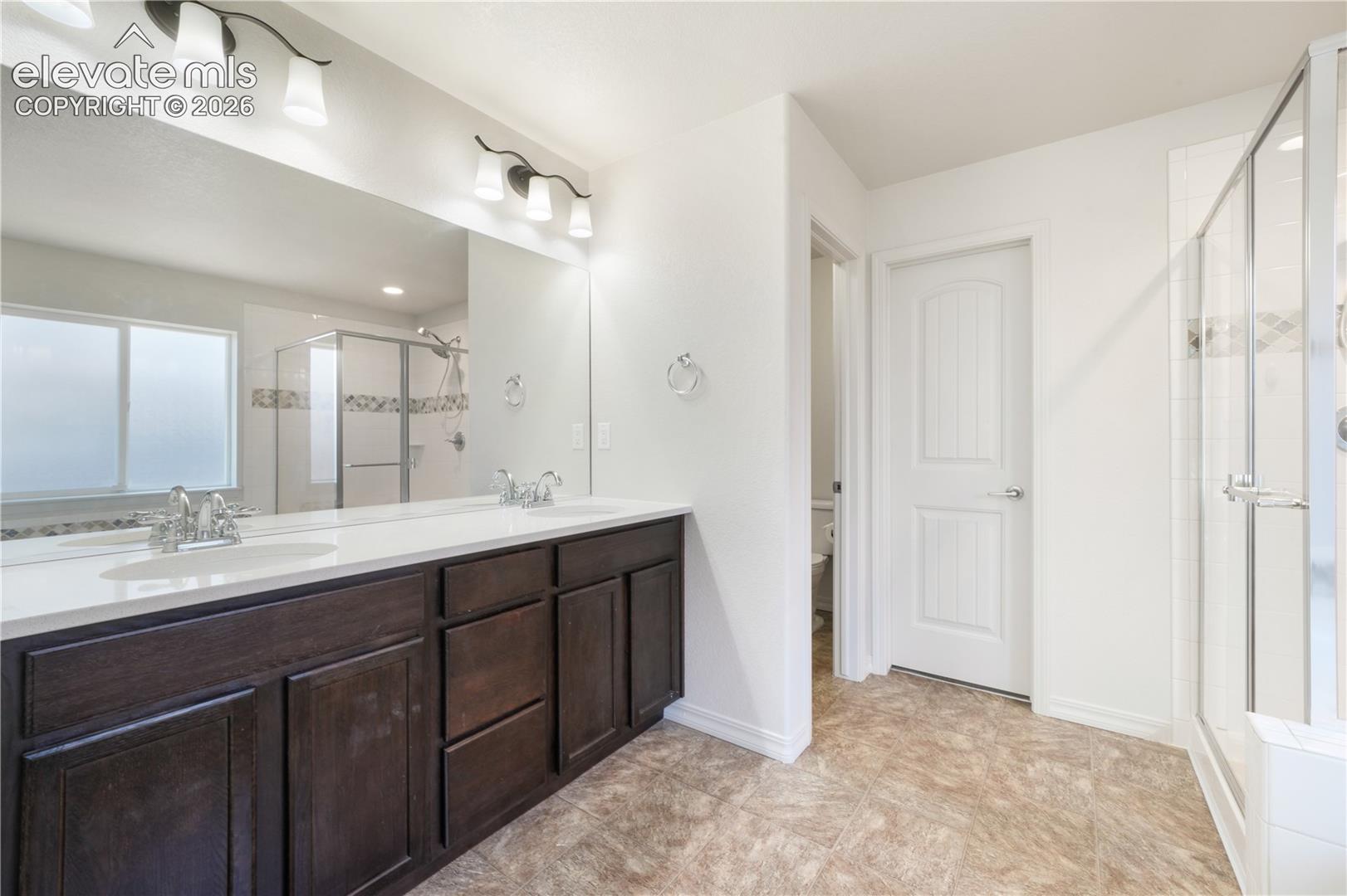 Main level primary 5 piece bathroom with dual sinks, granite counters, free standing shower, large bathtub, large walk in closet