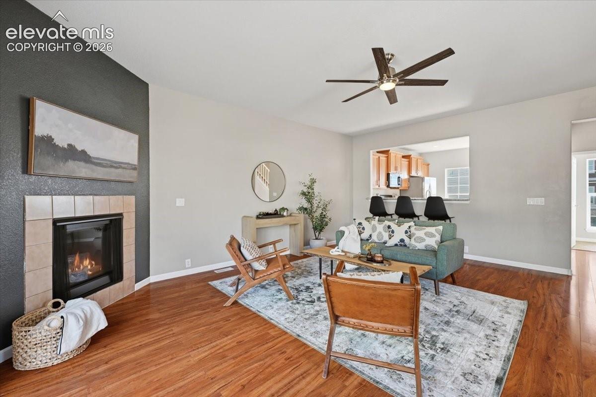 Hardwood flooring, tiled fireplace, ceiling fan, and a kitchen pass-through window