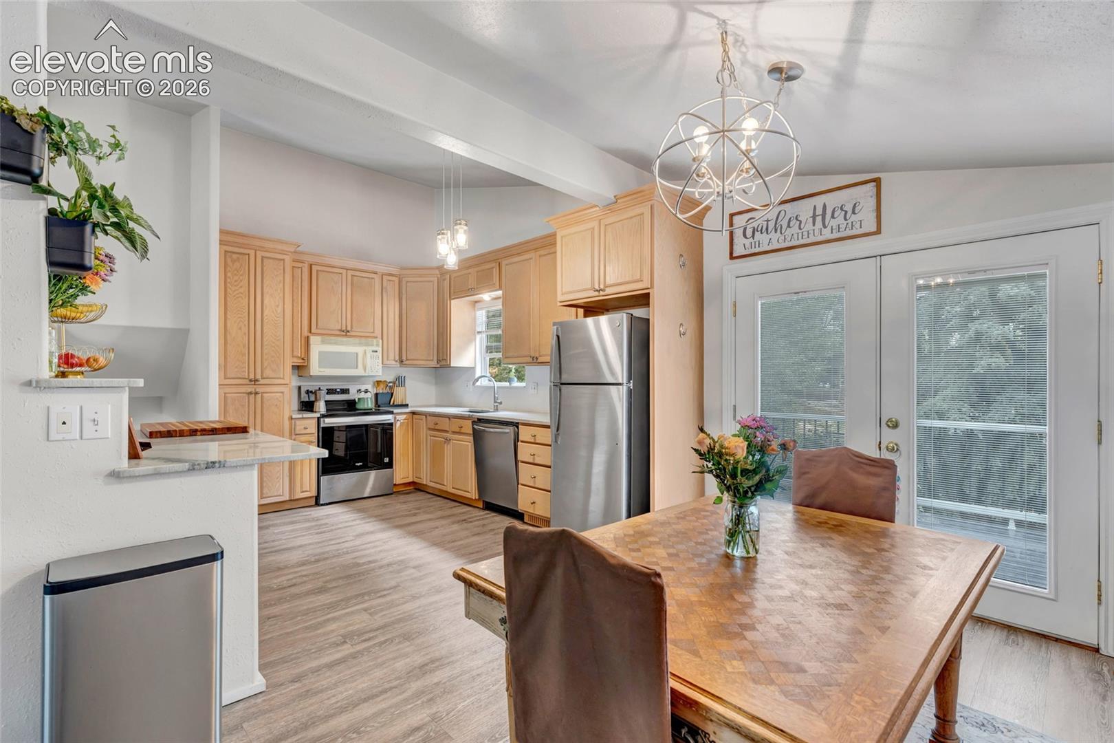 Open-concept kitchen and dining area featuring light wood-finish cabinetry, stainless steel appliances, and wood-finish flooring