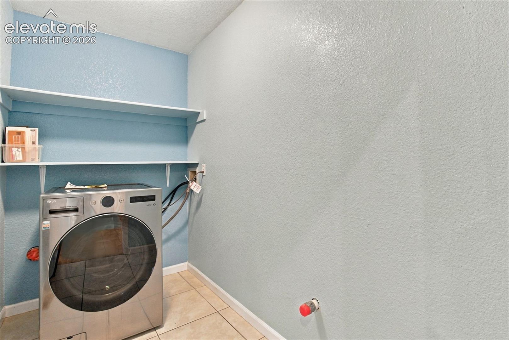 Dedicated main level laundry area featuring dual wall-mounted shelving and tile flooring and plumbed for a sink