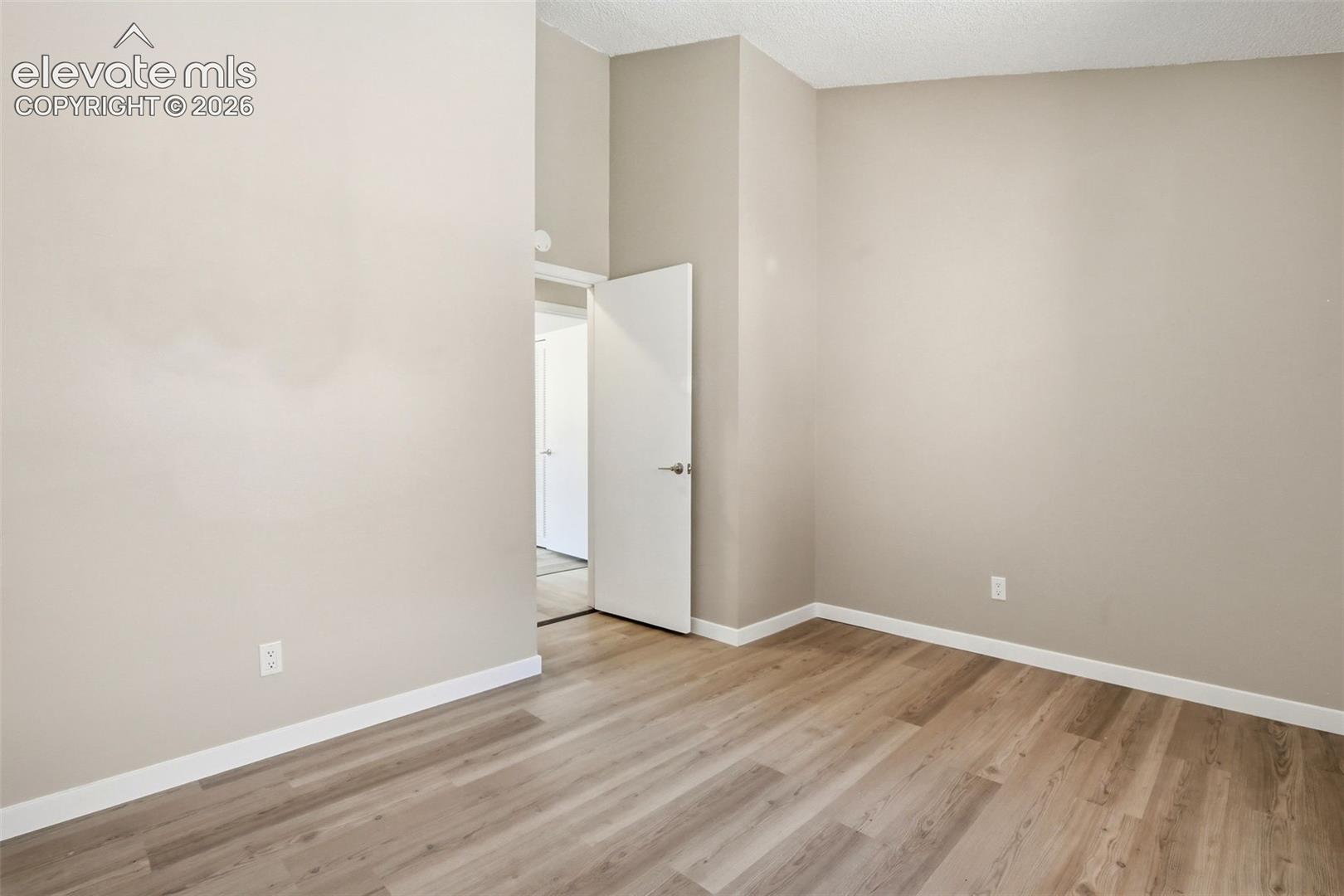 Spacious room featuring wood-finish flooring, light neutral wall tones, and white baseboards