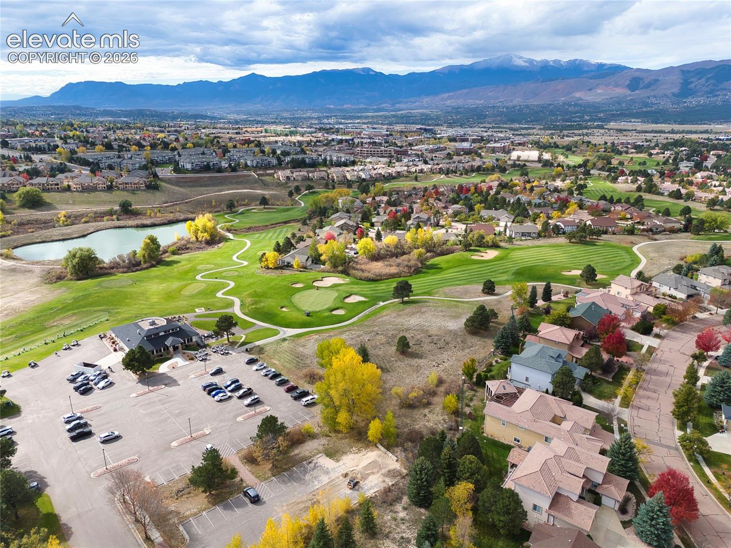 Aerial perspective featuring an expansive golf course, mature deciduous trees, a natural pond, and a backdrop of mountain ranges