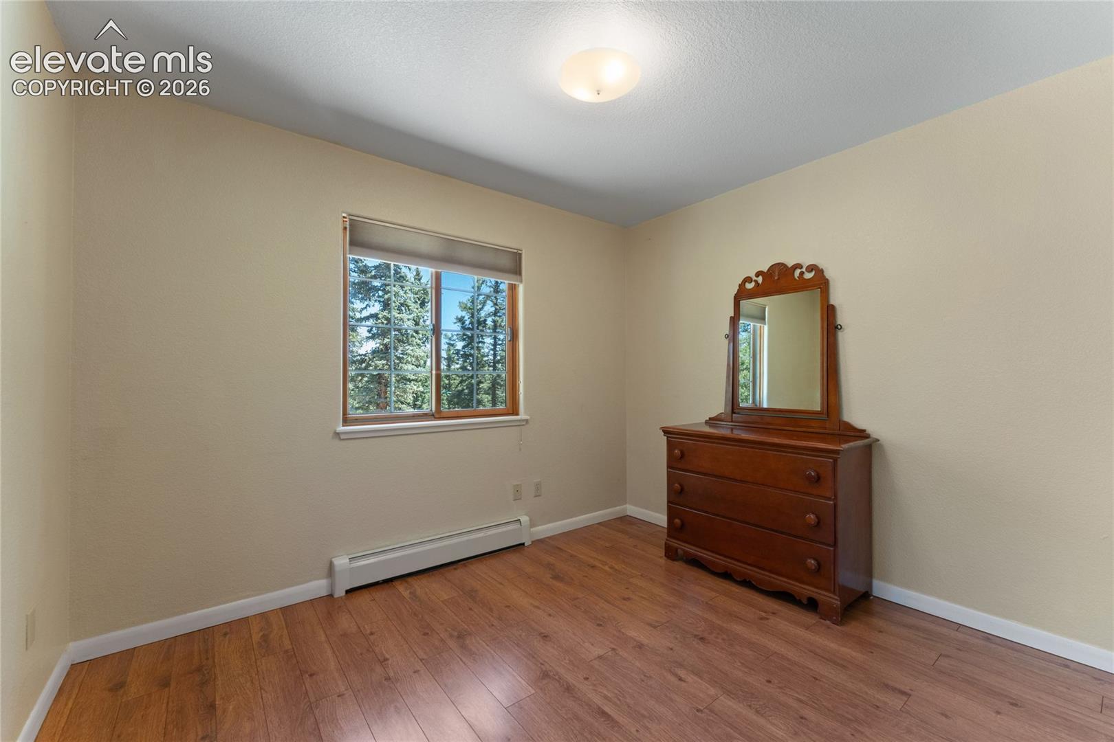 Room with wood-finish flooring, neutral wall paint, and a window with a natural wood frame