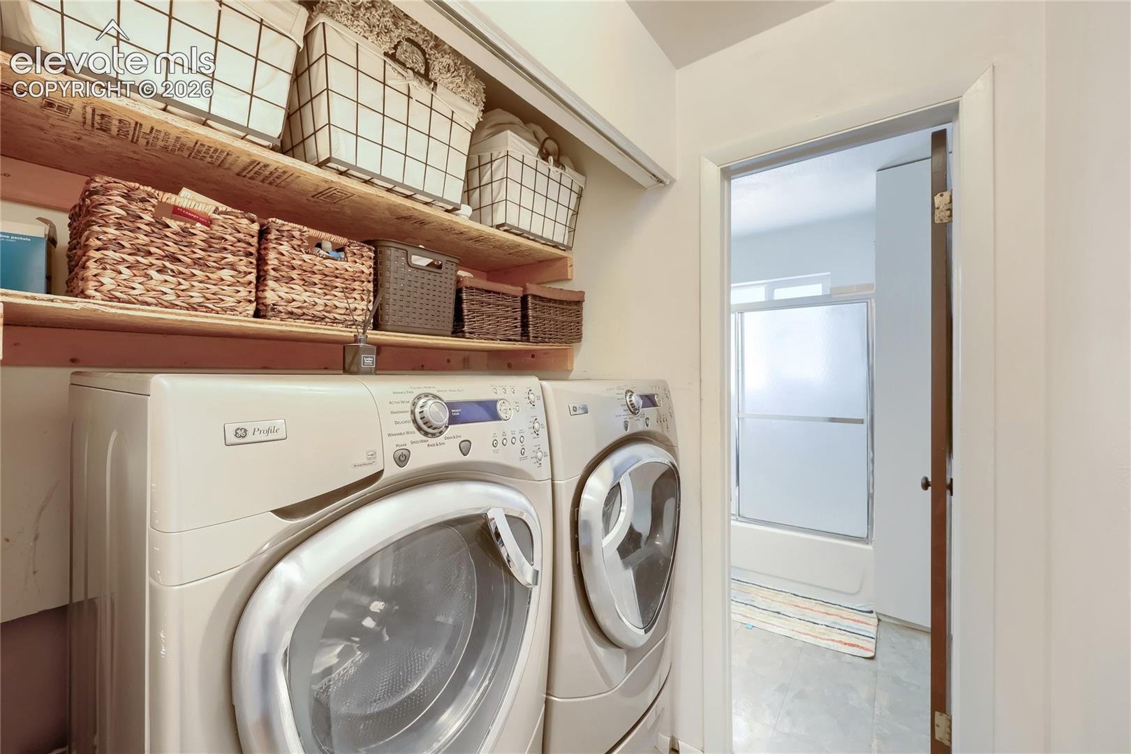 Laundry area featuring dual built-in wooden shelving units and an open doorway revealing a shower-tub combination with a white surround