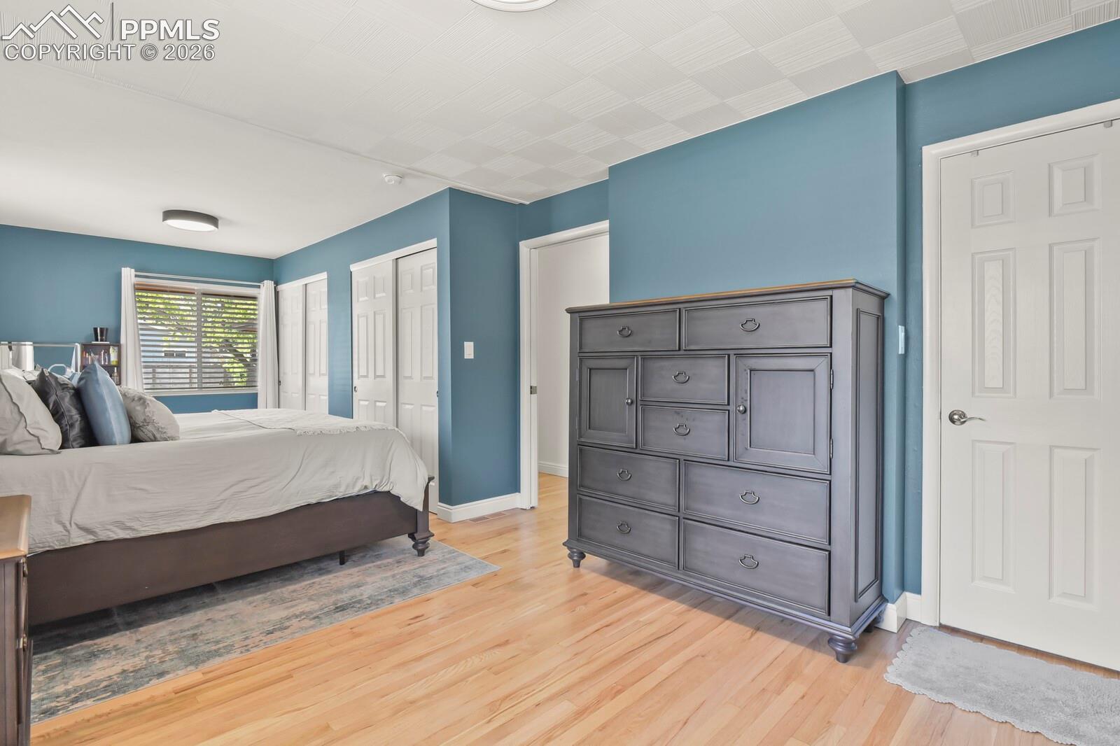 Spacious primary bedroom featuring hardwood flooring, double closets, multiple windows and private bathroom