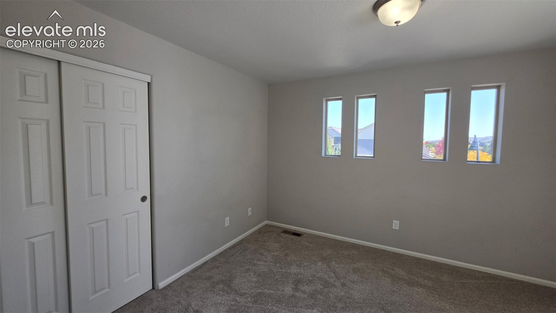 Neutral-toned interior featuring wall-to-wall carpeting, sliding closet doors with paneled detailing, flush-mount lighting, and four rectangular windows