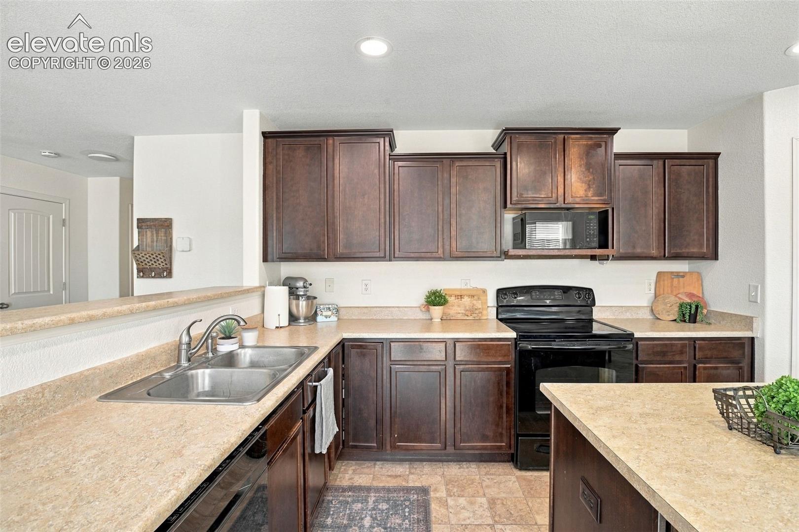 U-shaped kitchen featuring wood-finish cabinetry, a double basin sink, and an integrated black range with an overhead microwave