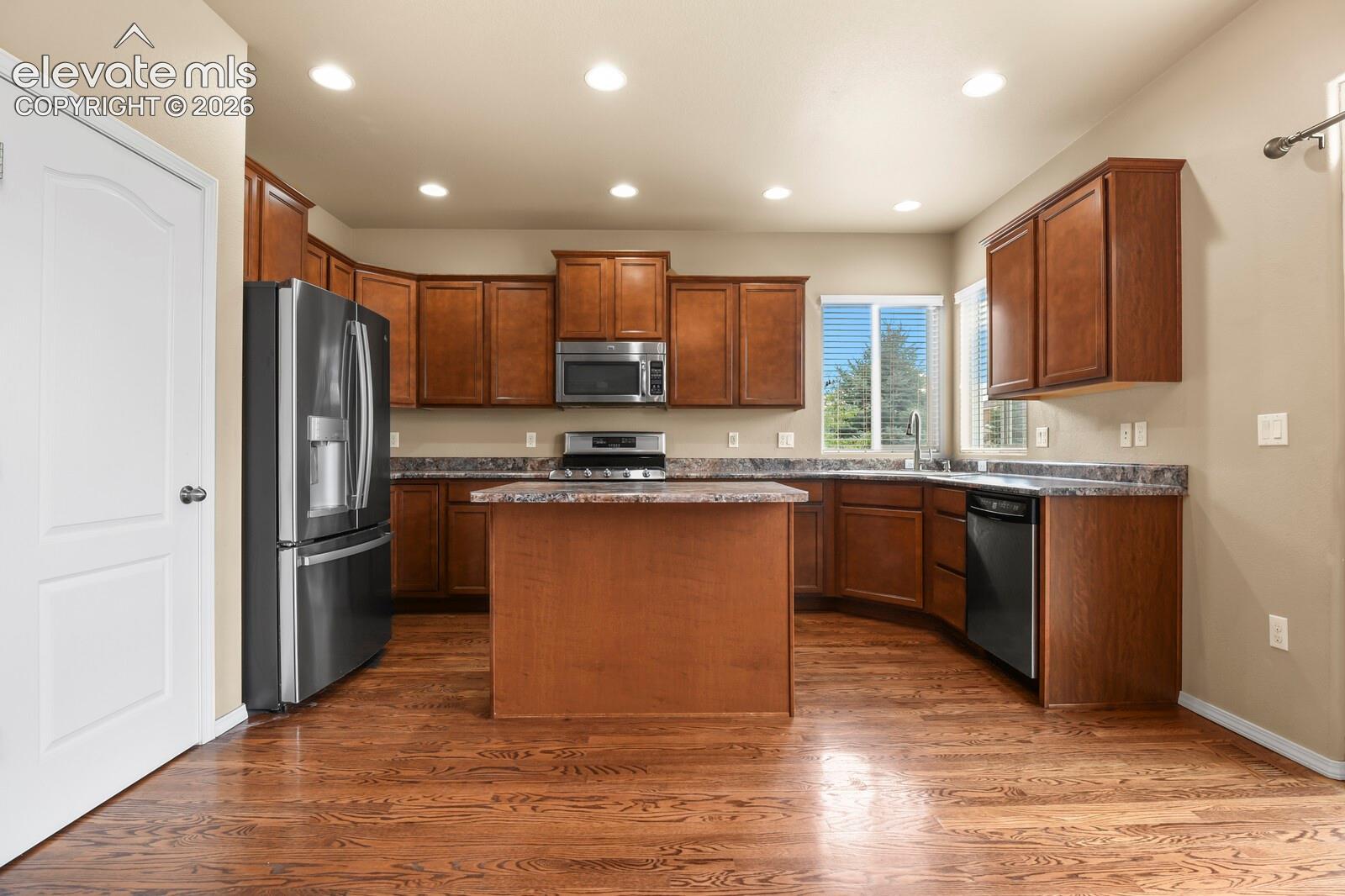 Kitchen featuring wood-finish flooring, an island, wood cabinetry, stainless steel appliances, and recessed lighting