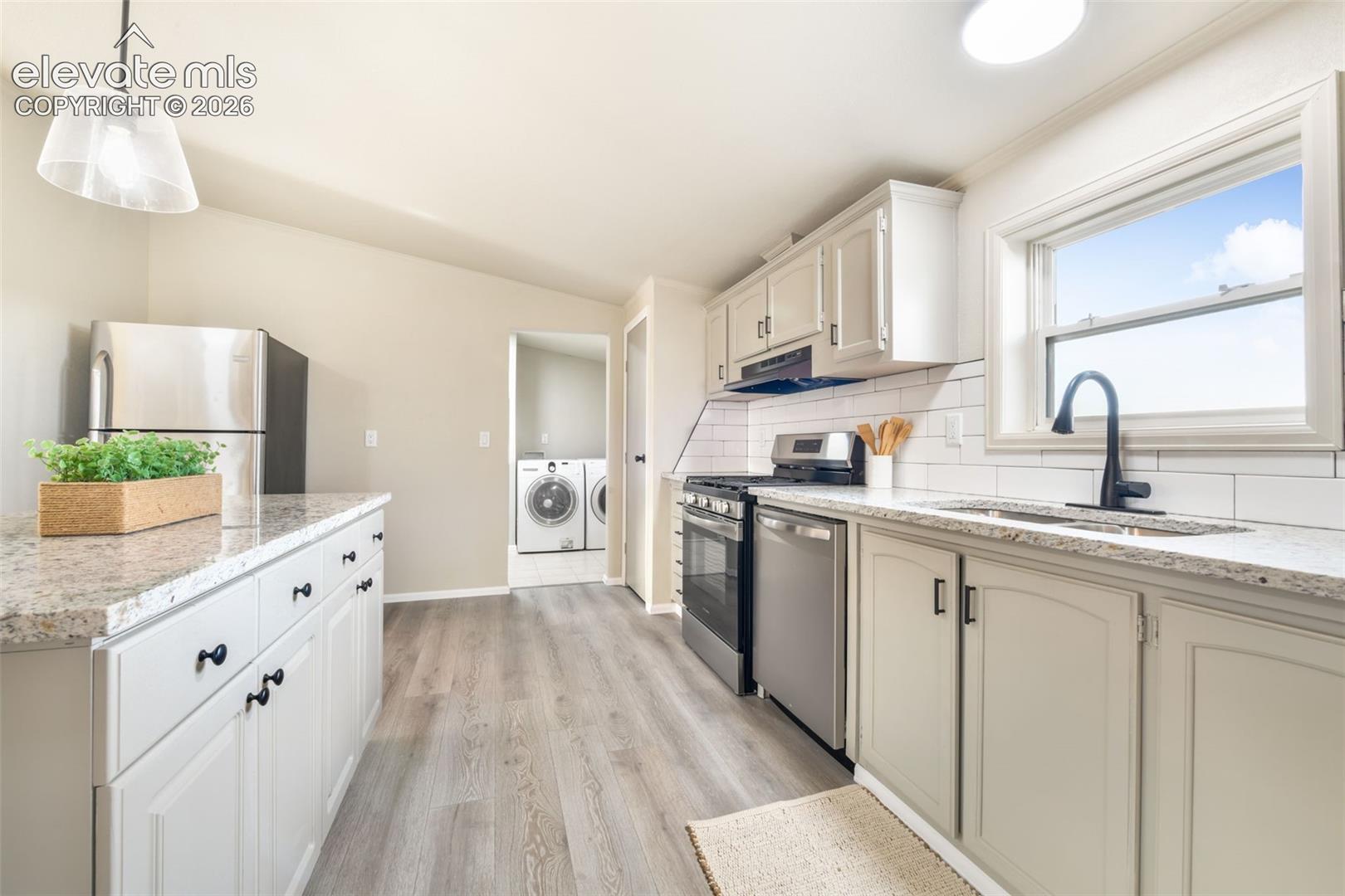 Kitchen featuring light-toned cabinetry, a white subway tile backsplash, stainless steel appliances, and a double basin sink with a matte black faucet