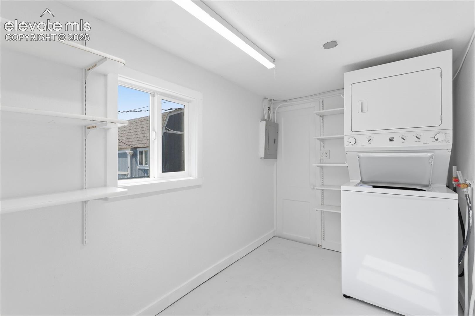 Laundry room featuring an integrated washer and dryer unit, built-in shelving, and a single window.