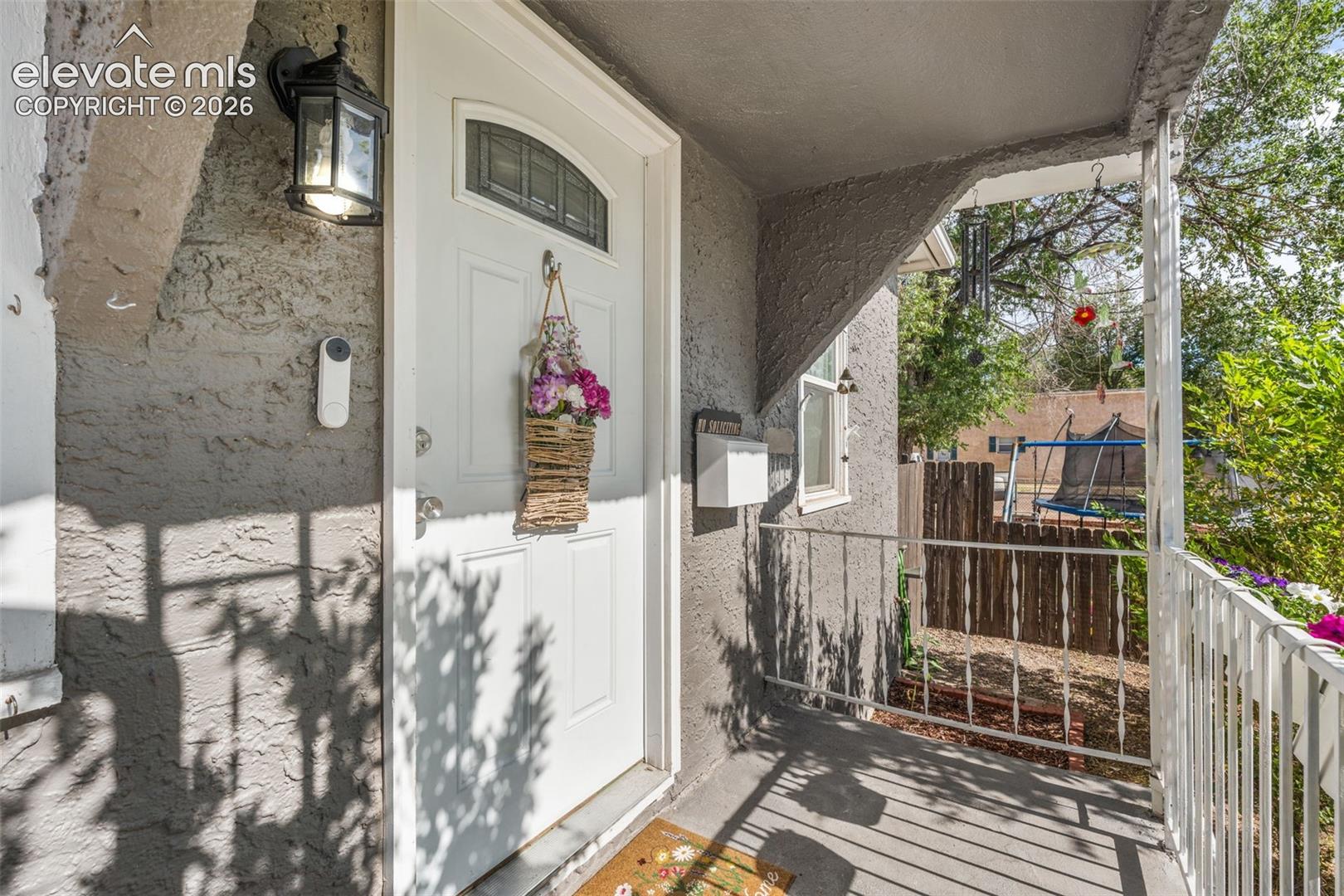 Front entry featuring a white door with an arched window insert, stucco exterior, and an exterior wall lantern