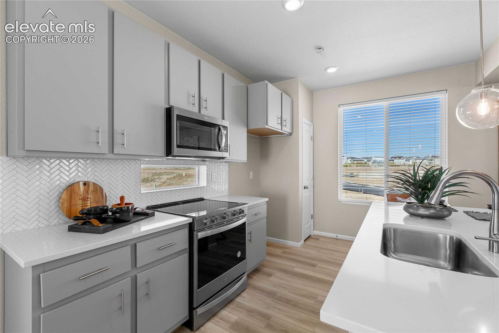 Kitchen featuring light gray cabinetry, white countertops, stainless steel appliances, a white herringbone tile backsplash, and wood-finish flooring
*photos of a model home*