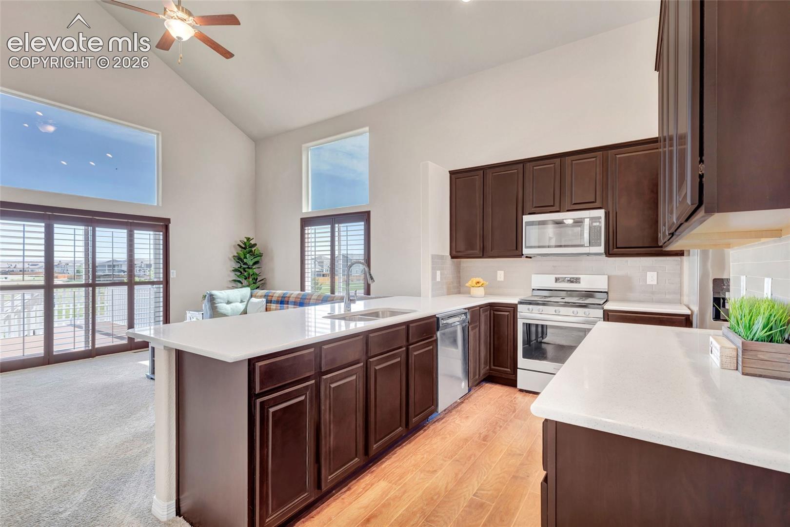 Open-concept kitchen featuring wood-finish flooring, white countertops, dark wood cabinetry, and stainless steel appliances