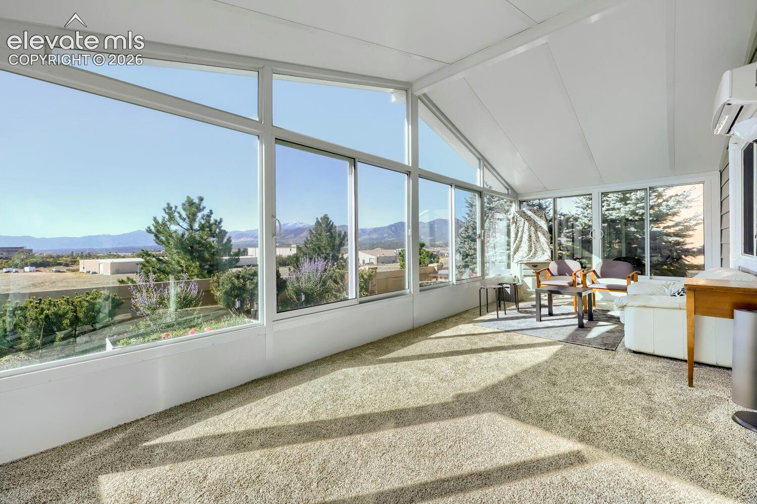Sunroom featuring expansive floor-to-ceiling windows, vaulted ceilings, wall-mounted climate control unit, and carpeted flooring