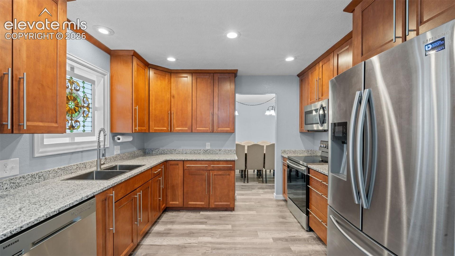 Kitchen featuring wood cabinetry, granite countertops, stainless steel appliances, and a double basin sink with a high-arc faucet