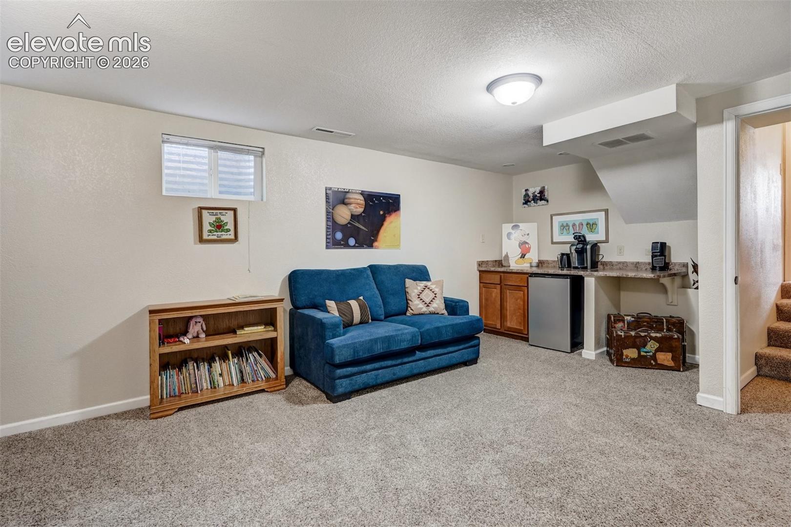 Carpeted room featuring a built-in wet bar with wood-finish cabinetry, a mini-refrigerator, and a stone-finish countertop