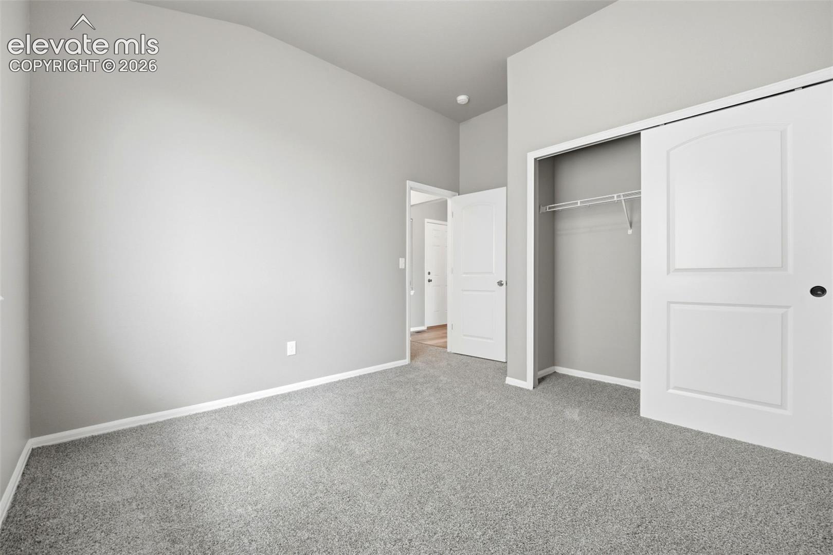 Vaulted ceiling, neutral gray wall tones, gray carpeting, white trim, and a built-in closet with sliding doors