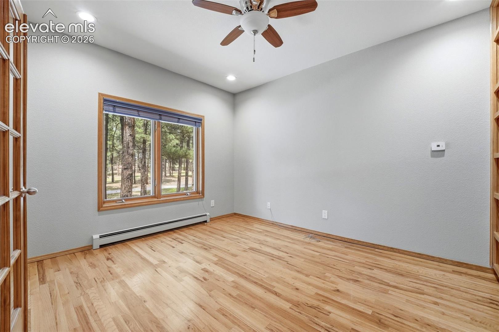 Room featuring wood-finish flooring, a wood-framed window with a tree-lined backdrop, and a ceiling fan