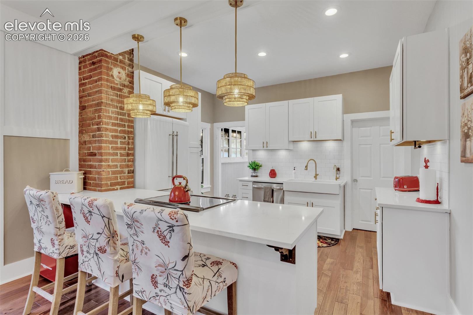 Open-concept kitchen featuring white cabinetry, a large kitchen island with counter seating, a white apron-front sink, and rich wood-finish flooring