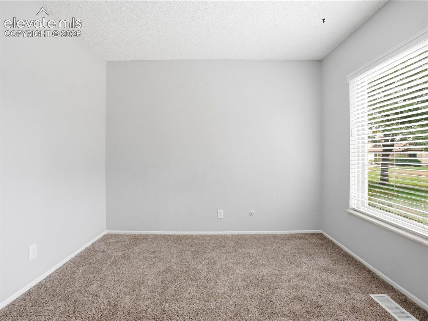 Neutral-toned room featuring neutral carpeting, light-colored walls, and a large window equipped with horizontal blinds