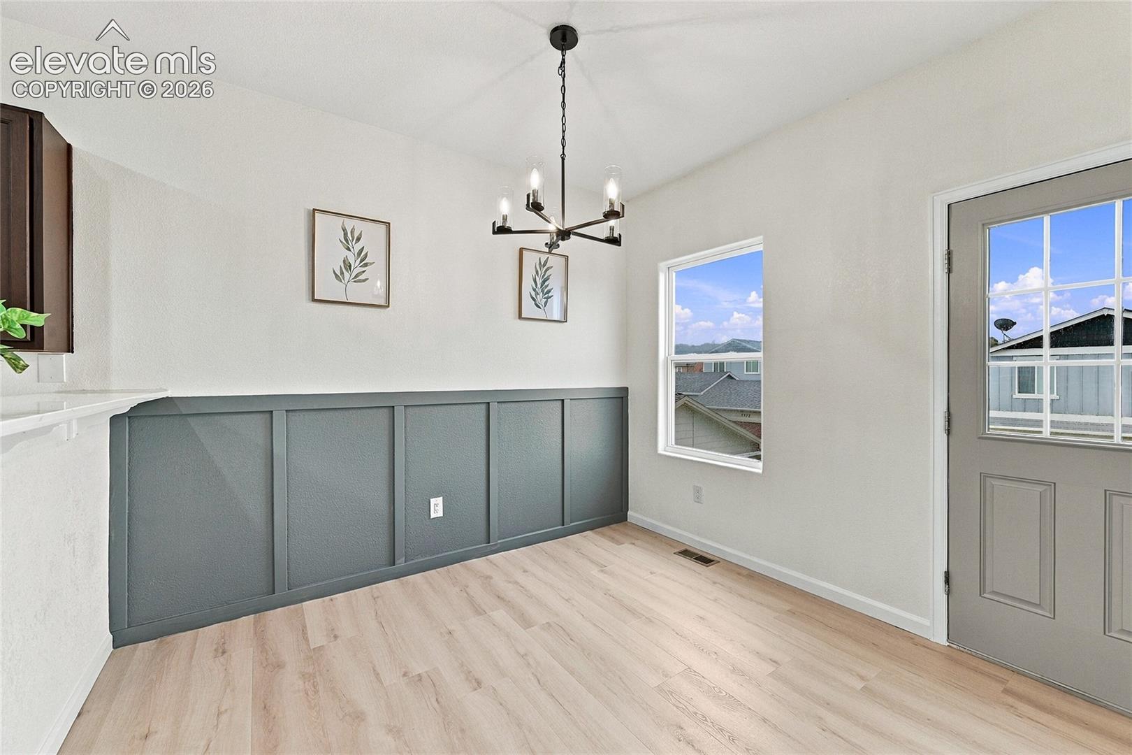 Interior space featuring wood-finish flooring, a charcoal-toned wainscoting accent wall, a multi-arm chandelier, and an exterior door with integrated glass panels