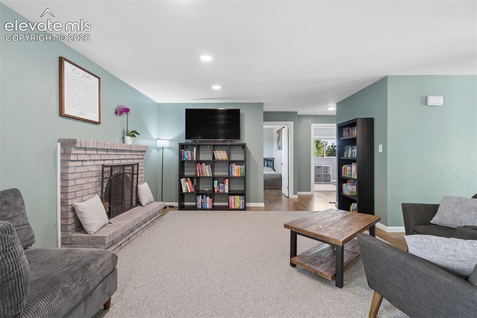 Living area featuring a floor-to-ceiling brick fireplace with a raised hearth, recessed lighting, and neutral carpeting