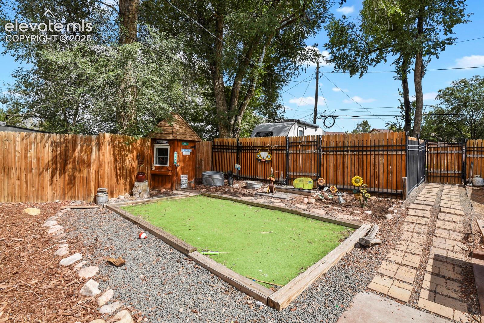 Enclosed outdoor area featuring a manicured artificial turf patch, a wooden playhouse, a full privacy fence, and a paver pathway