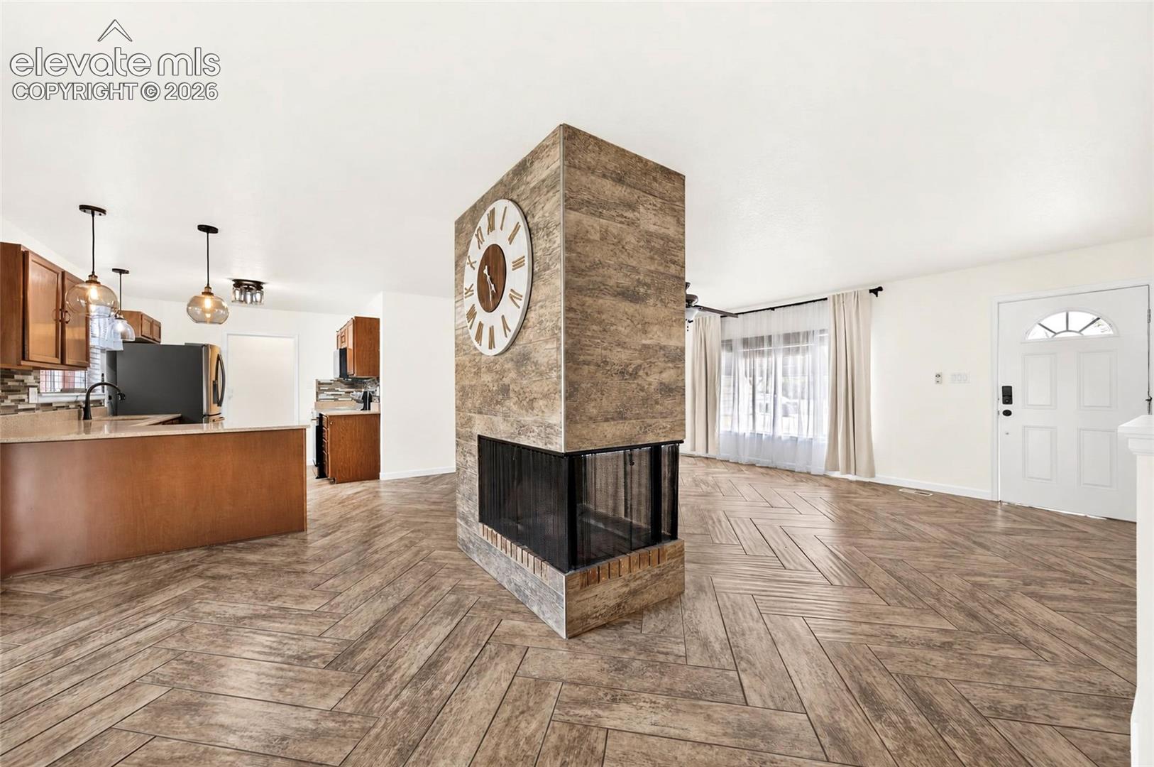 Double-sided, tile-clad fireplace feature with a wood-finish, herringbone-patterned floor, wood cabinetry, and pendant lighting