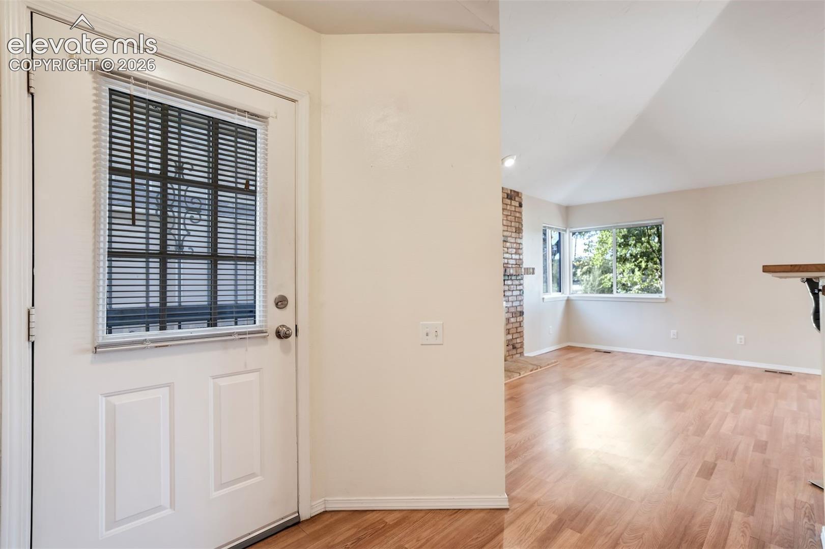 Entrance featuring a white door with an integrated glass panel, wood-finish flooring, vaulted ceilings, and a floor-to-ceiling brick hearth