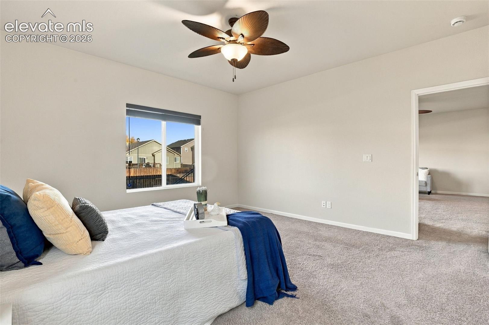 Neutral-toned interior space featuring wall-to-wall carpeting, a multi-blade ceiling fan with integrated light fixture, and a single-hung window with a dark frame
