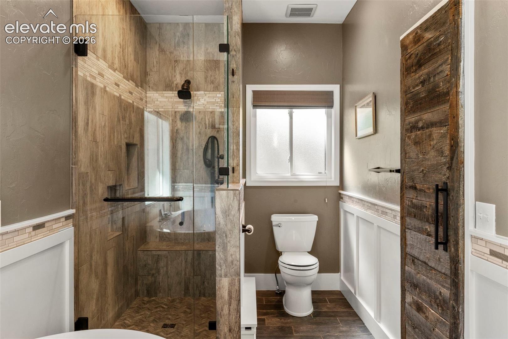 Bathroom featuring a textured wall, a shower stall, wood tiled floors, and a wainscoted wall