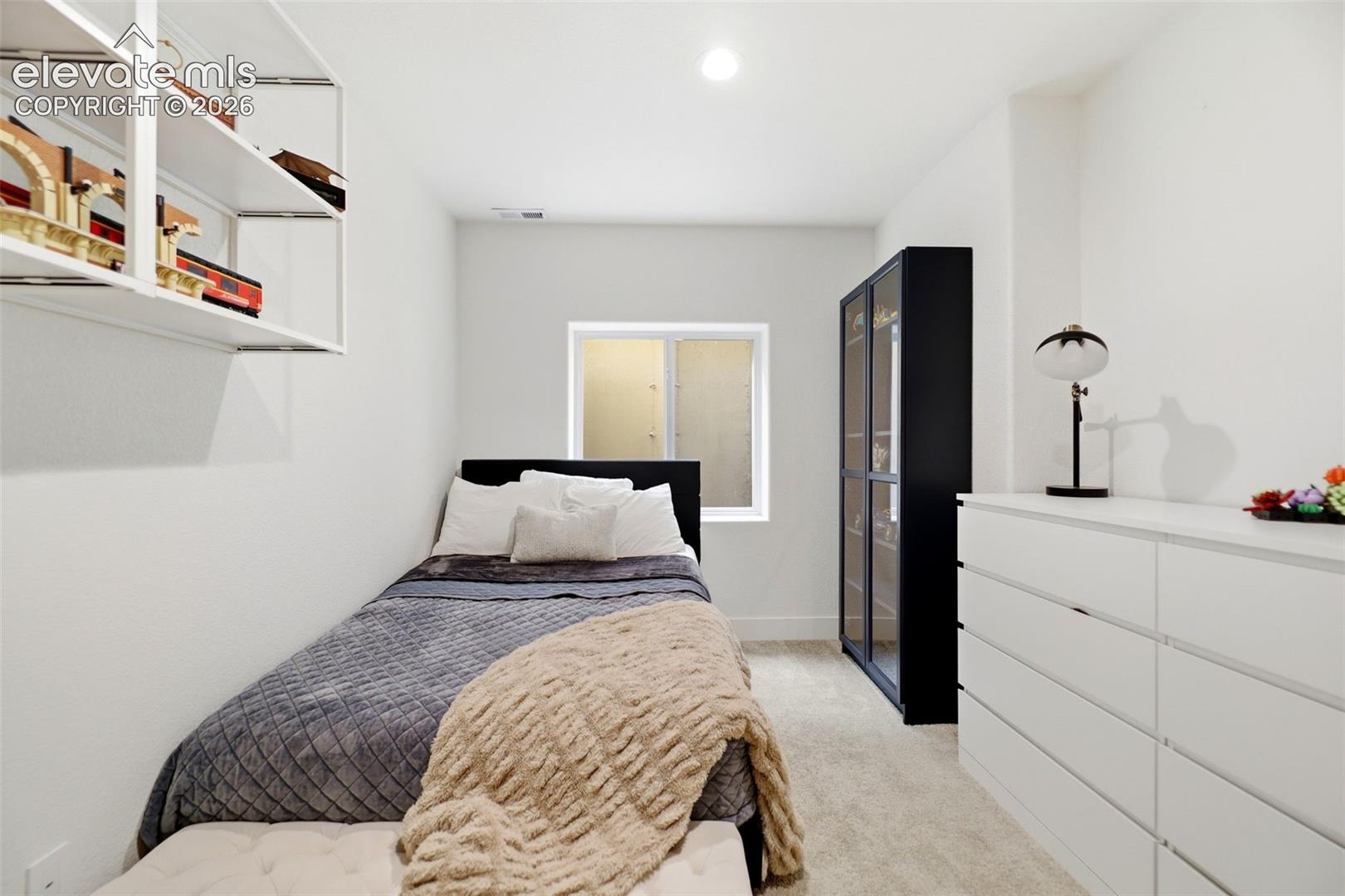 Recessed ceiling lighting, wall-mounted open shelving, a window with a frosted glass panel, and light-toned carpeting