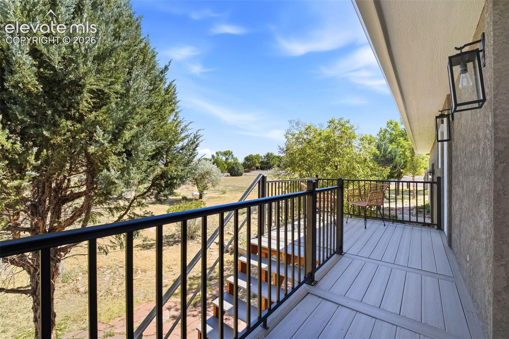 Exterior balcony featuring a composite deck, black metal railings, and dual outdoor wall lanterns