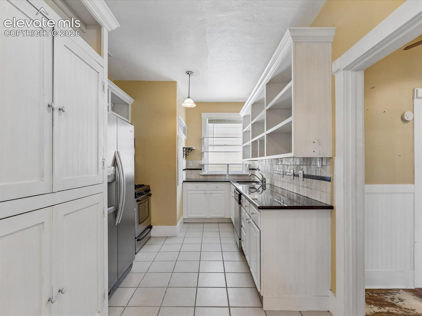 Kitchen featuring white cabinetry, tile flooring, dark countertops, a stainless steel refrigerator, and a stainless steel range