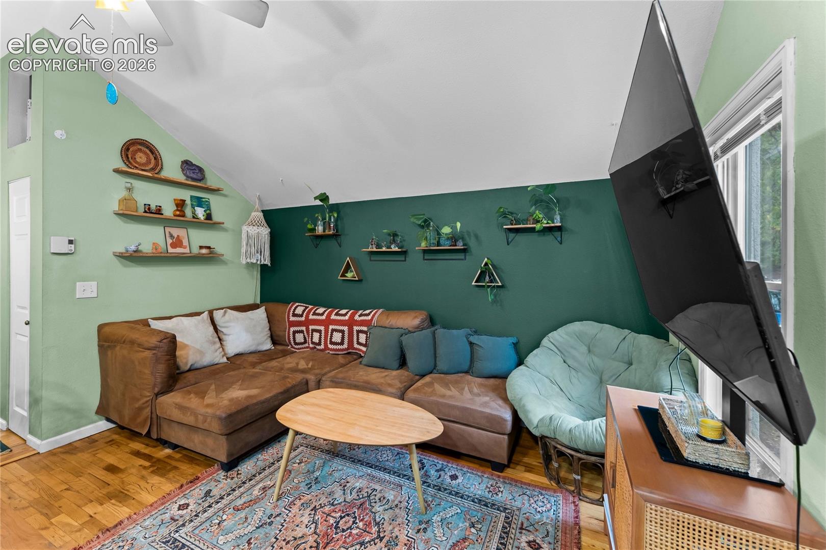 Vaulted ceiling featuring a central paddle fan, wood-finish flooring, and multiple wall-mounted floating shelves