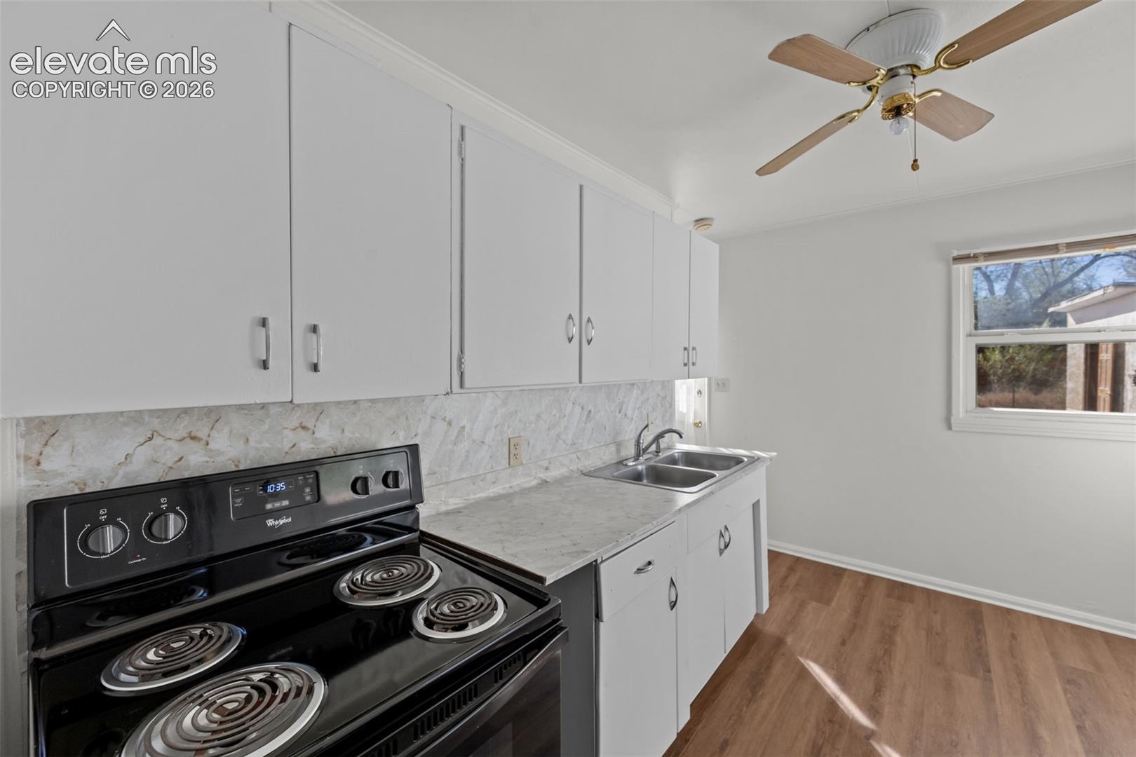 Kitchen featuring white cabinetry, stone-patterned laminate countertops, tile backsplash, stainless steel double-basin sink, and wood-finish flooring
