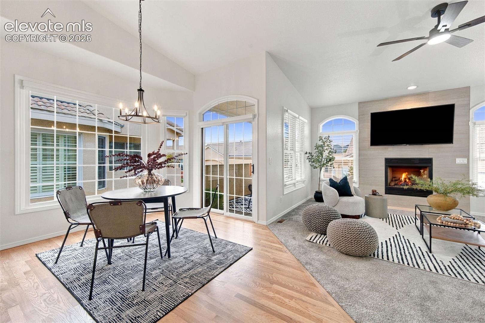 Open-concept interior featuring vaulted ceilings, floor-to-ceiling fireplace with stone-finish surround, wood-finish flooring, sliding glass door, and large picture windows with arched detailing