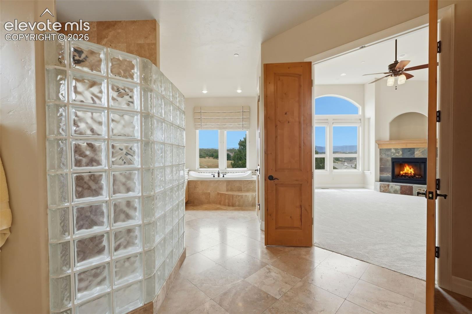 Glass block shower enclosure with a built-in soaking tub, tile flooring, and light wood doors