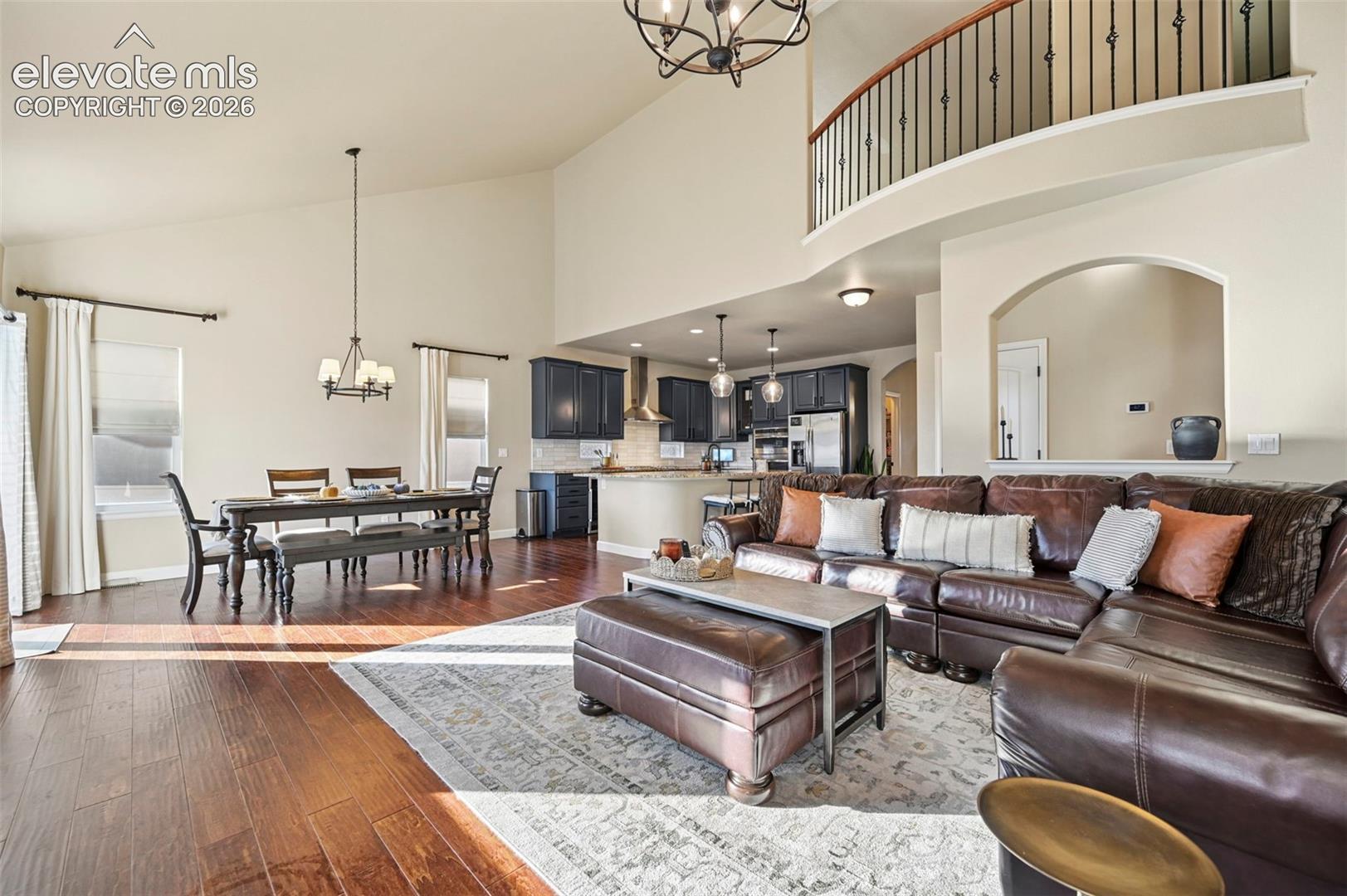 Open-concept living area with vaulted ceiling, wood-finish flooring, and a kitchen featuring dark cabinetry and a breakfast bar